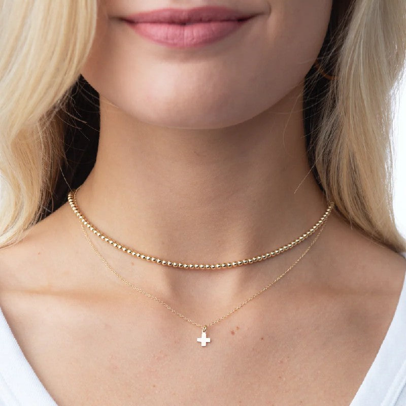 Close-up of a person wearing a gold necklace with a cross pendant.