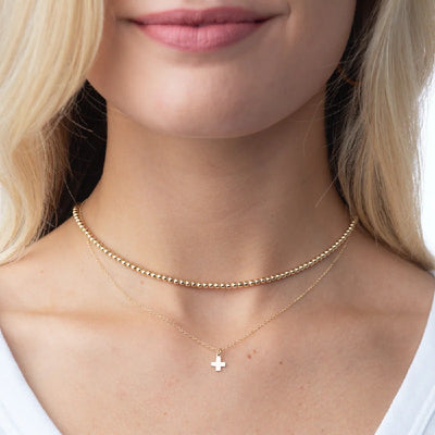 Close-up of a person wearing a gold necklace with a cross pendant.