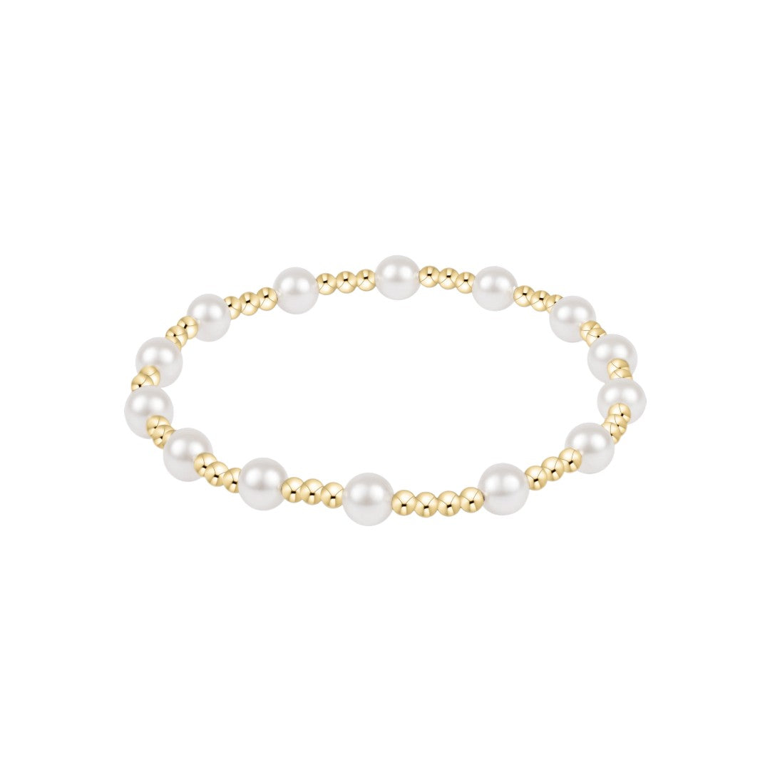 A delicate beaded bracelet featuring alternating large white pearls and small polished gold beads, arranged in a horizontal oval on a solid white background.