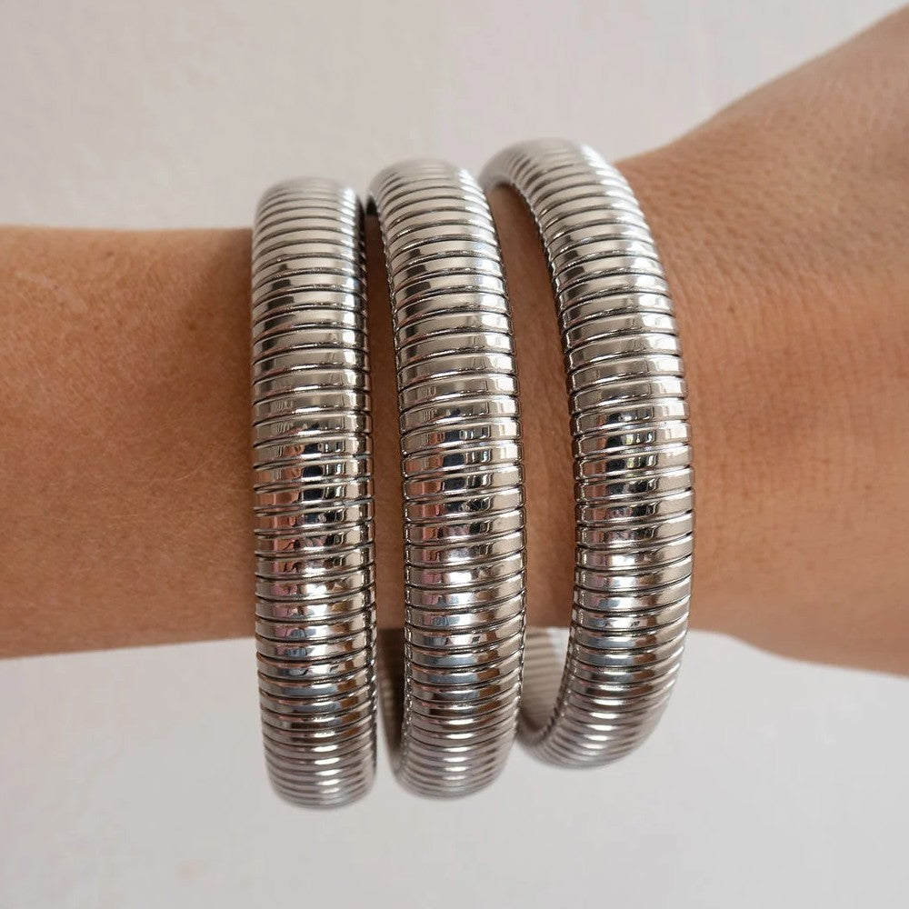 Three wide, ribbed silver metal bangles wrapped on a person's wrist against a plain light background.