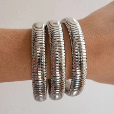 Three wide, ribbed silver metal bangles wrapped on a person's wrist against a plain light background.