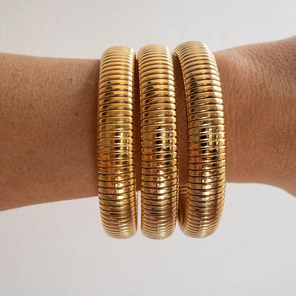 Three gold-plated snake-bone style bangles stacked together on a person's wrist, shown against a plain light background.