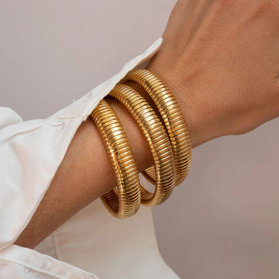 Gold fluted bracelet stack on arm with gray background.