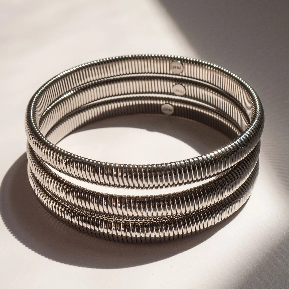 A stack of three silver-toned metal bangles with a textured, ridged exterior, displayed on a light surface with dramatic shadows.