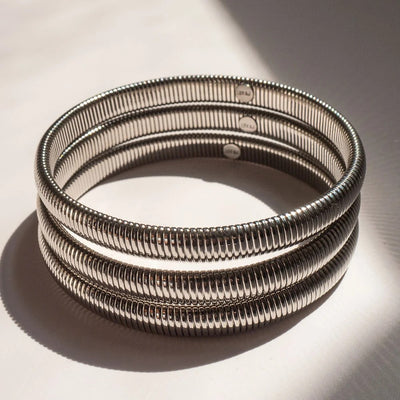 A stack of three silver-toned metal bangles with a textured, ridged exterior, displayed on a light surface with dramatic shadows.