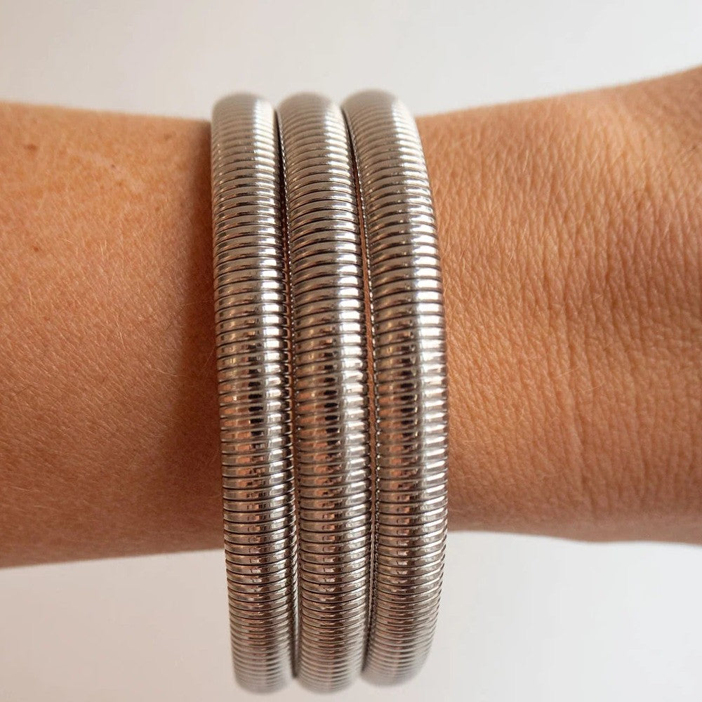 Three slim metallic bangles with a textured, ribbed snake-like pattern worn on a person's wrist against a plain light background.
