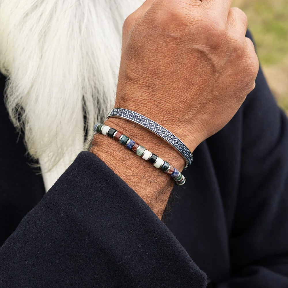A close-up of a person's wrist wearing two bracelets: a silver-toned geometric patterned band and a beaded bracelet with silver, white, red, and dark beads.